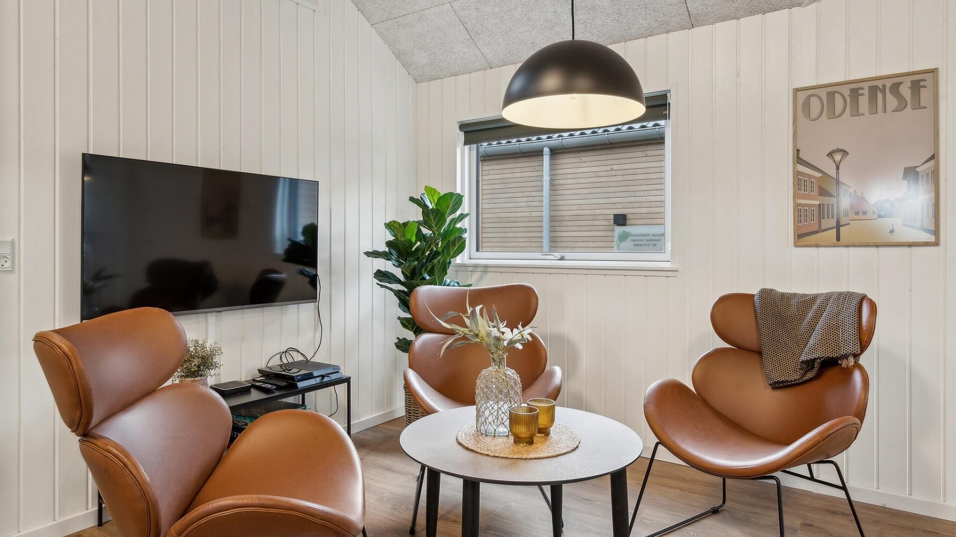 Un salon moderne doté d’un téléviseur à écran plat, de fauteuils en cuir, d’une table basse ronde et d’un grand luminaire suspendu.