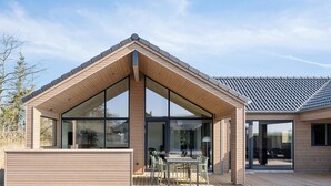 A modern house with a wooden exterior, large glass windows, and a covered patio area with outdoor furniture. - VillaVilla 648 - Hasmark Strand, Fyn og øer (Otterup)