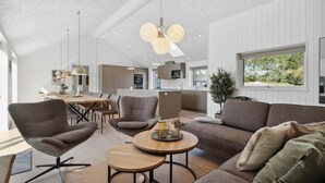 A modern interior with a dining area, a living room with a sofa and armchairs, and a kitchen in the background.