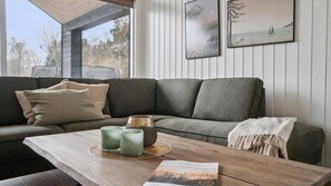 Uma sala de estar moderna com um sofá seccional, uma mesa de centro de madeira com objetos decorativos e obras de arte emolduradas na parede.