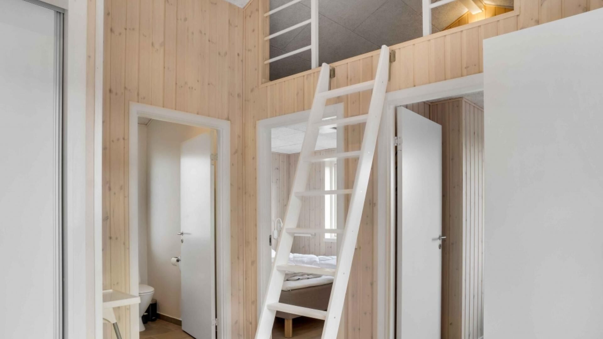 A room with wooden walls, a white door, and a white ladder leading to a loft area.
