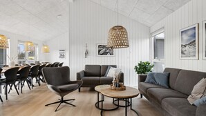 Uma sala de estar moderna com um sofá cinza, uma mesa de centro redonda e uma área de jantar com cadeiras e mesa.
