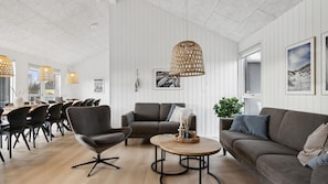 A modern living room with a sofa, armchairs, a coffee table, and a dining area with chairs and a table.