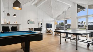 Um quarto espaçoso com mesa de bilhar, mesa de tênis de mesa e uma grande janela com vista para o exterior.