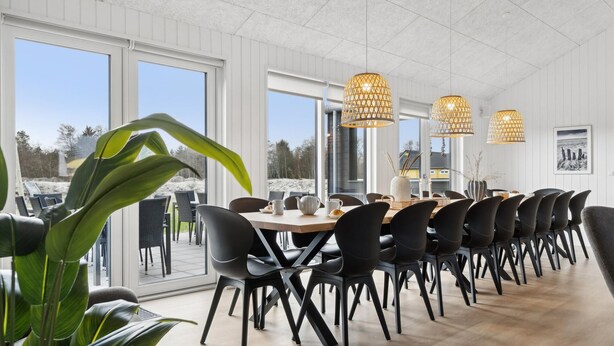 Uma área de refeições moderna com uma mesa comprida, cadeiras pretas e luminárias pendentes.
