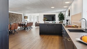 Een moderne keuken met een centraal eiland, een eetgedeelte met een accentmuur van steen, en een woonruimte met een grote televisie.