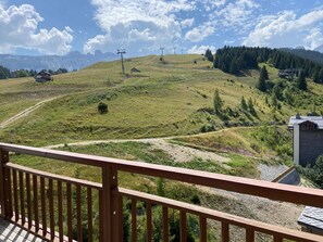 A mountainous landscape with a wooden deck overlooking a grassy hill.