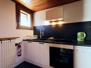 Eine kompakte Küche mit schwarzem Arbeitsplatz, einer Edelstahl-Spüle, einem grünen Wasserkocher, einem eingebauten Backofen und einem Fenster über der Spüle.