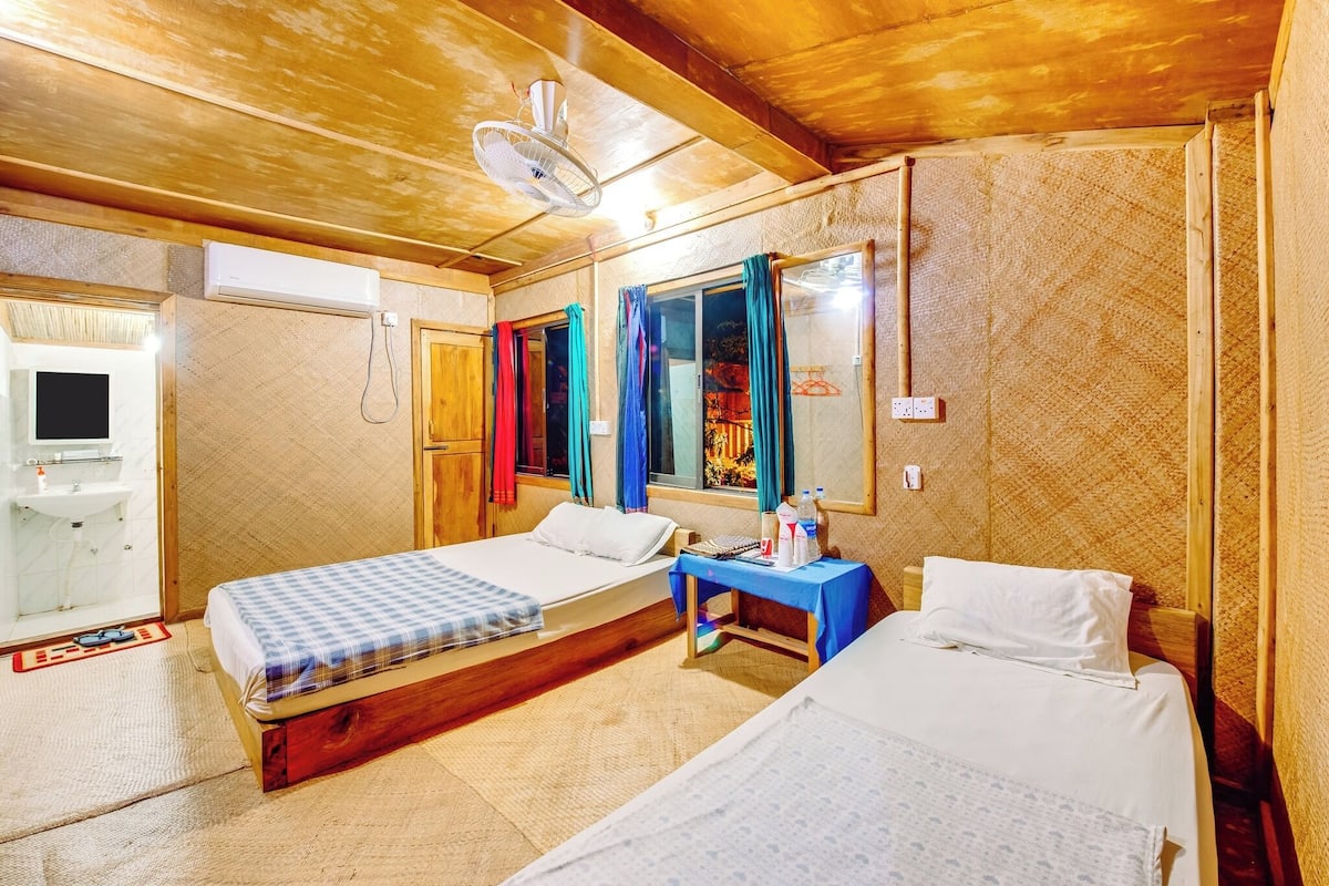 A room with two beds, a small table, a mirror, and a window with curtains.