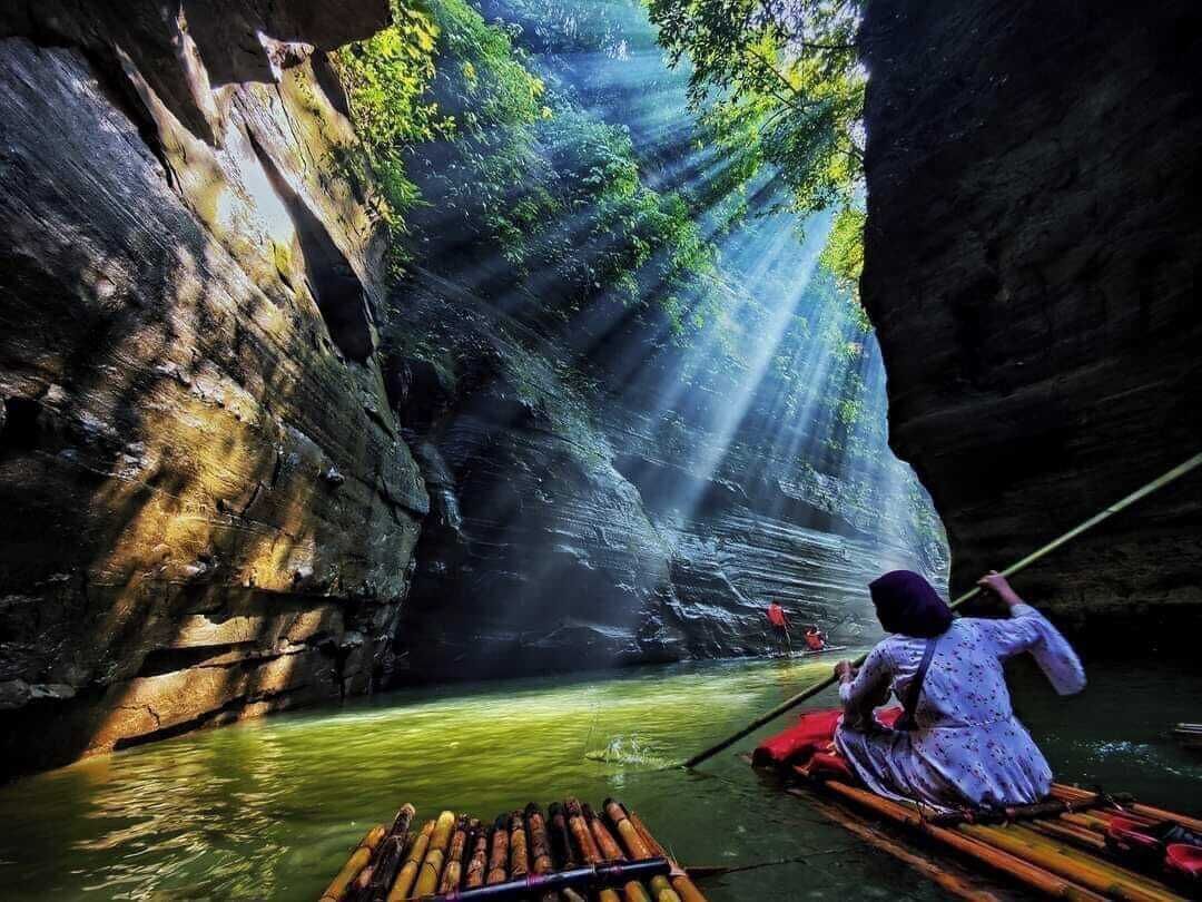 A narrow waterway with a rocky wall on one side and a person paddling a boat.