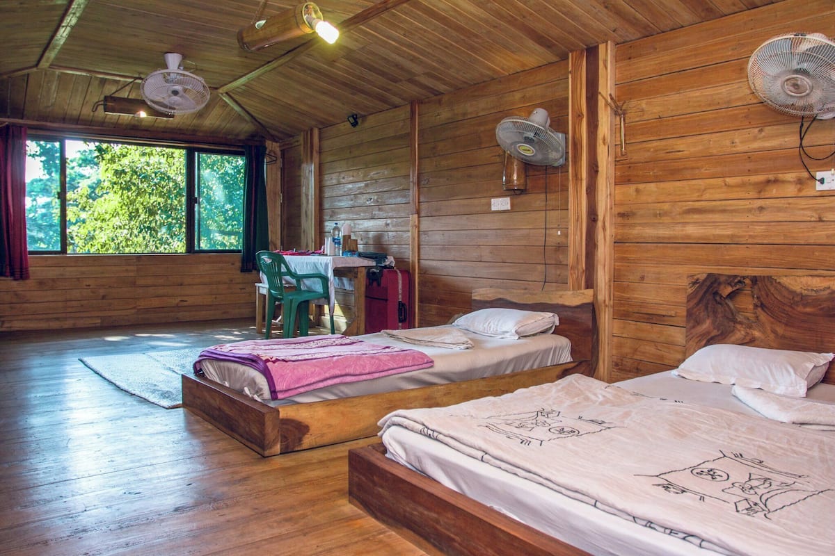 A wooden cabin with two beds, a desk, and a chair.