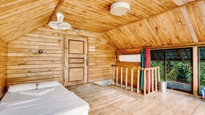 A wooden cabin with a bed, a small balcony, and a sliding glass door leading to a garden.