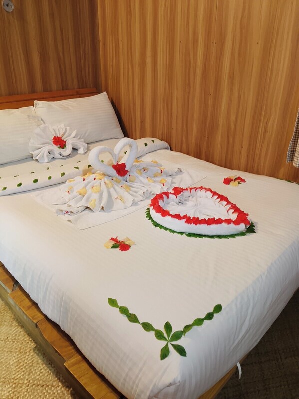 Uma cama bem arrumada com colcha floral, almofada decorativa e toalha dobrada em formato de cisne.