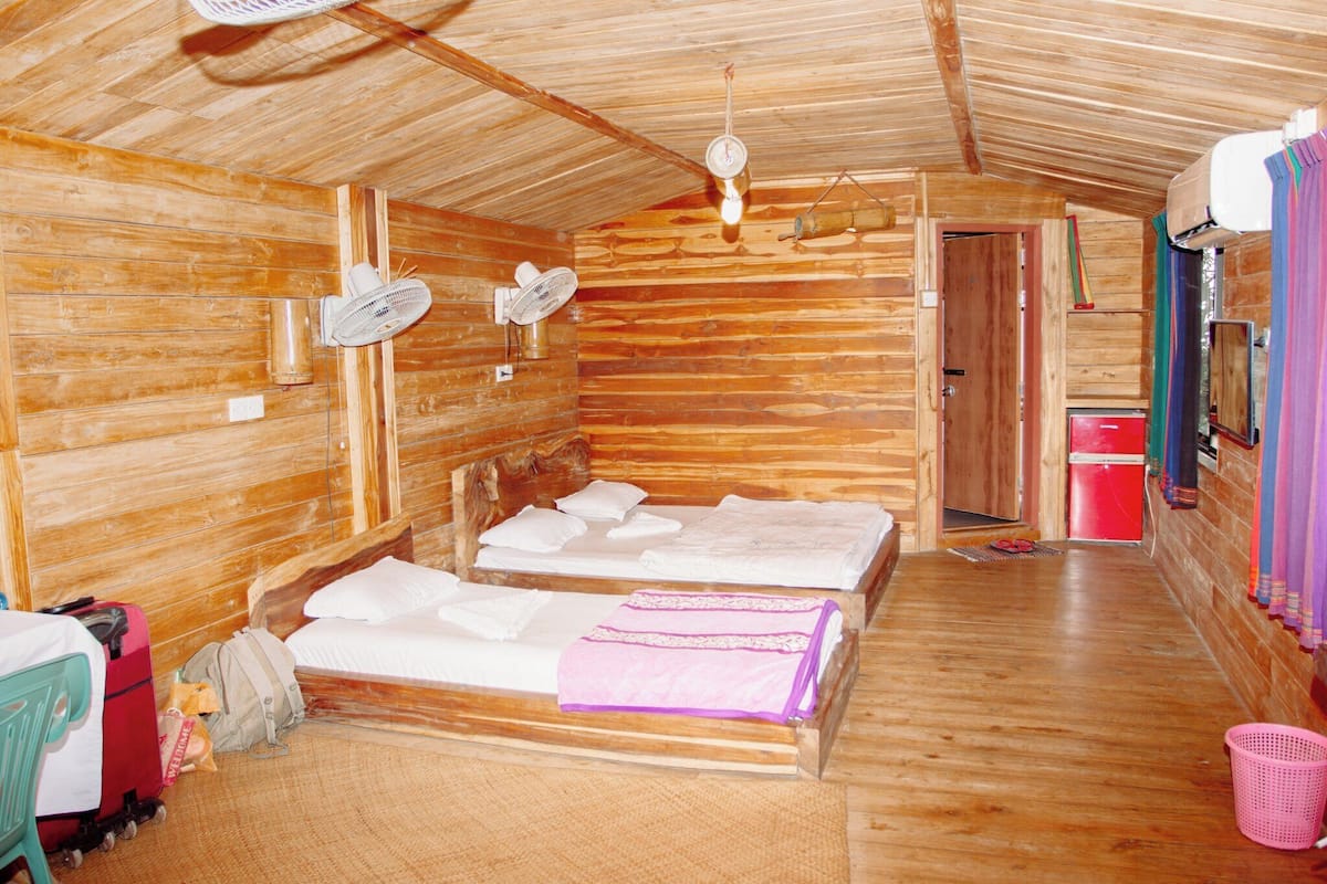 A wooden cabin with two beds, a fan, a heater, and a small kitchenette.