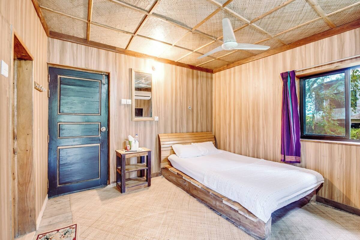 A wooden room with a bed, a nightstand, a ceiling fan, and a window with curtains.