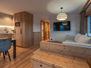 Un dormitorio moderno con una cama de madera, un televisor montado en la pared y una zona de cocina con armarios de madera y un microondas.