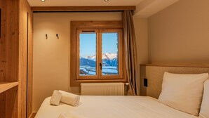 Una camera d'albergo con un letto grande, testiera in legno, una finestra con vista su montagne innevate e un armadio in legno.