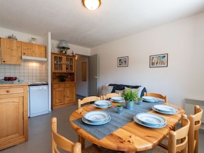 A compact kitchen with wooden cabinets, a dishwasher, and a dining table set for six with blue plates. - Cozy duplex for 4 people, near shops and ski slopes (Saint-Lary-Soulan)