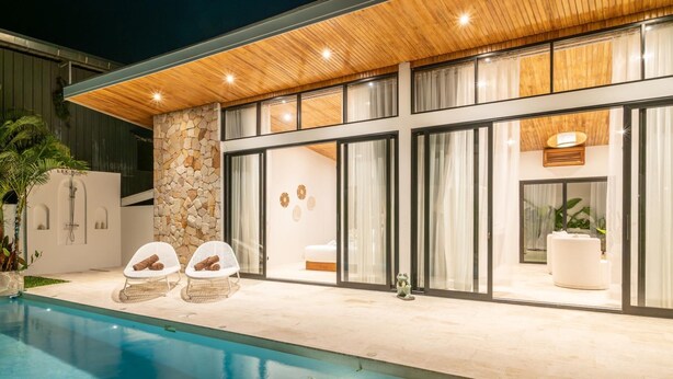 Una casa moderna con piscina, muro de piedra y ventanas amplias.