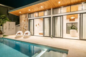 Una casa moderna con piscina, muro de piedra y ventanas amplias.