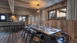 Interior rústico de madera con una larga mesa de comedor dispuesta para seis personas, rodeada de sillas modernas.