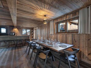 A rustic wooden interior with a long dining table set for six, surrounded by modern chairs.