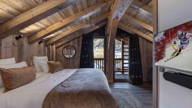 Un dormitorio acogedor con techo de madera, una cama con ropa de cama blanca y marrón, un espejo redondo y un televisor en la pared.
