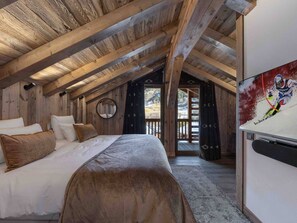 A cozy bedroom with a wooden ceiling, a bed with white and brown bedding, a round mirror, and a television on the wall. - Chalet in Méribel Raffort - 10 people, Pets allowed, Parking (Méribel)