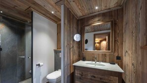 Un baño con detalles de madera, cabina de ducha de vidrio, inodoro blanco y tocador con espejo.