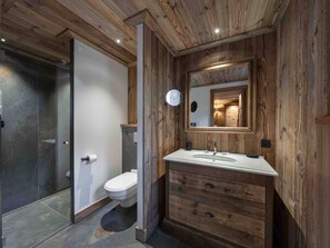 Une salle de bain avec un intérieur en bois, une douche en verre, des toilettes blanches et un meuble-lavabo avec un miroir.