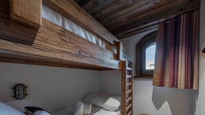 Una cama litera de madera con una escalera, un taburete pequeño y una ventana con cortinas.