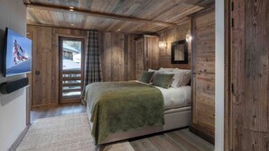 A cozy wooden room with a bed, a television on the wall, and a door leading outside.