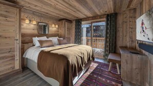 A wooden cabin bedroom with a bed, a TV, and a view of a snowy deck.