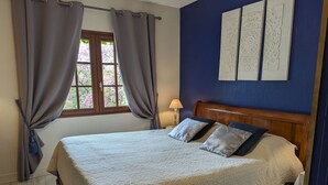 Quarto com cama de madeira, cortinas cinzas, janela com vista e duas obras de arte penduradas na parede.
