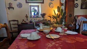 Mesa de jantar posta com pratos, copos e talheres, rodeada por cadeiras e uma janela com vista.
