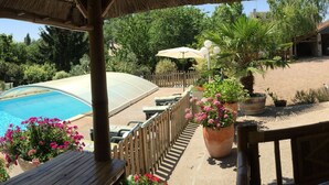 Un área de piscina con muelle de madera, sillas de descanso y una estructura de techo de paja.