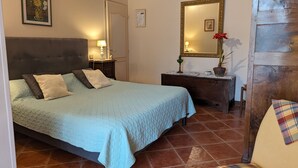 Un dormitorio con cama, mesita de noche, lámpara, cómoda, espejo y una silla.