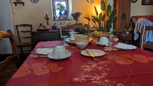Una mesa de comedor dispuesta con platos blancos, una copa de vino y una vela, rodeada de sillas y un aparador de madera.