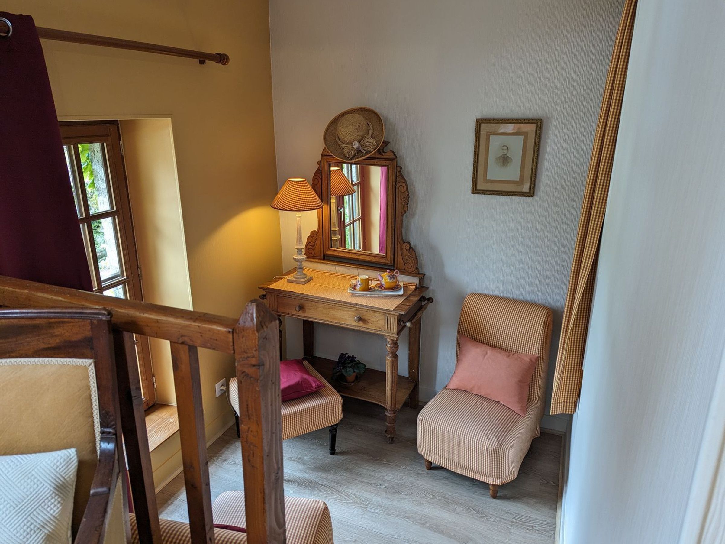Une pièce avec un bureau en bois, une chaise, un miroir, un tableau encadré et une fenêtre.