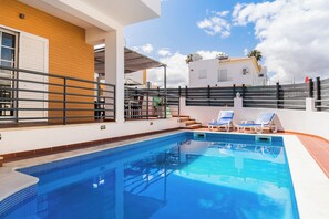 A swimming pool with lounge chairs, a wooden wall, and a white building in the background. - Solis Villa, Albufeira, Algarve (Albufeira)