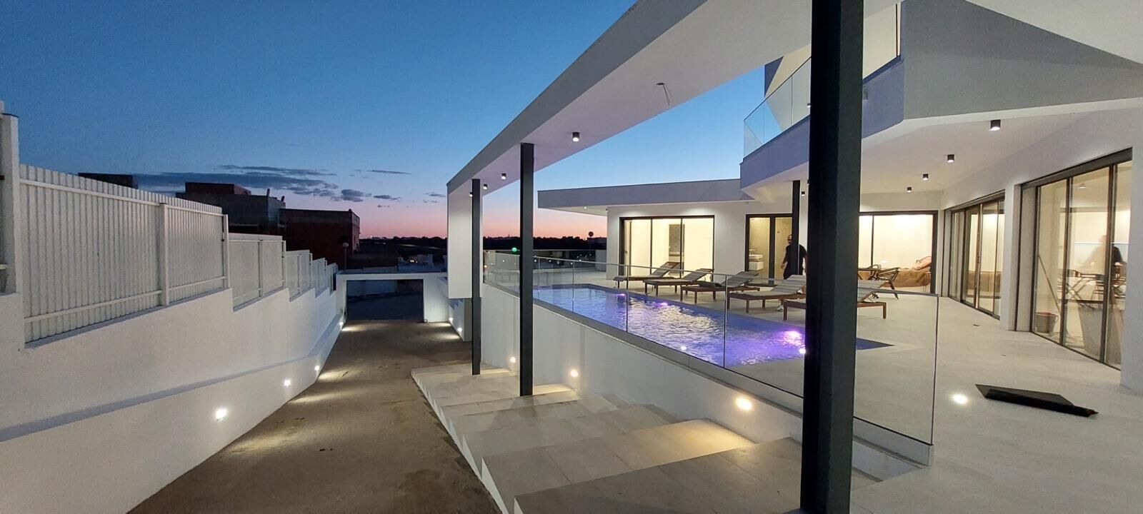 A modern rooftop pool area with glass railings and a clear view of the sky.