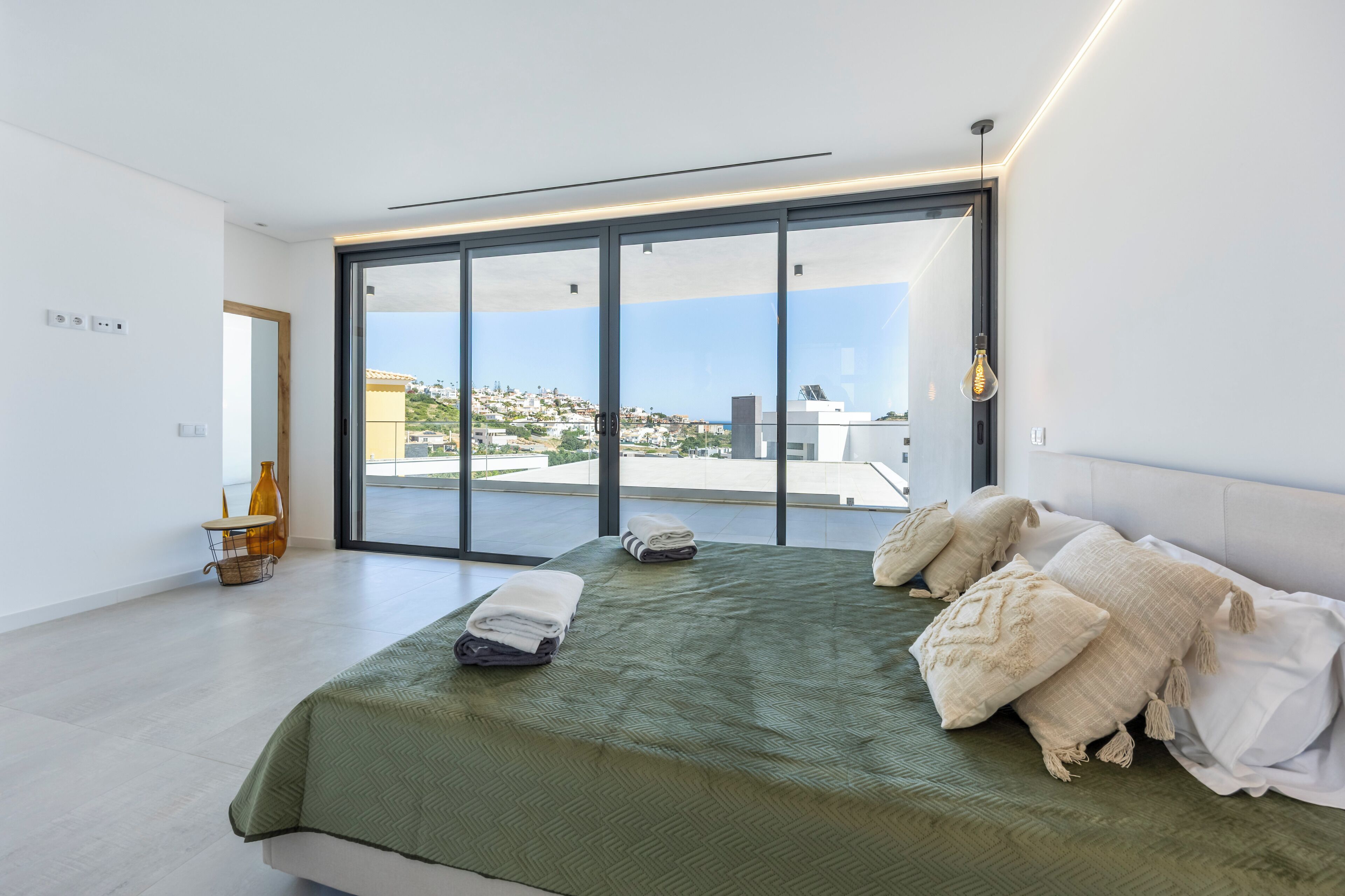 A modern bedroom with a large bed, a view of the city, and a balcony.