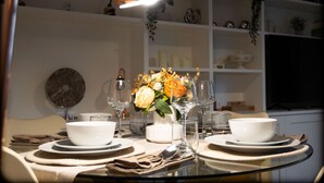 Una mesa de comedor dispuesta con platos, tazones y vasos blancos, un florero con flores y una lámpara colgante.
