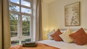 Habitación de hotel con un ventanal grande, una cama con muchos cojines y un cuadro en la pared.
