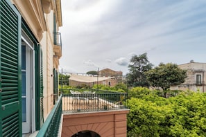 A balcony with a table and chairs, a green railing, and a view of surrounding buildings and greenery.
