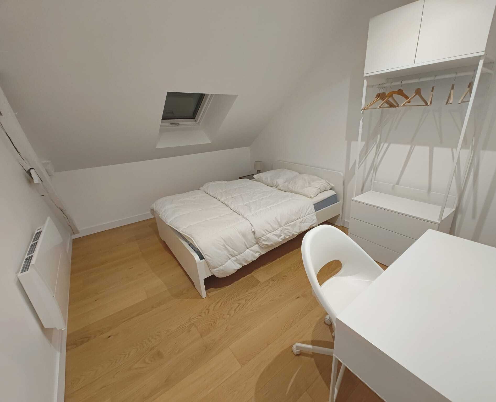 Une petite chambre à coucher blanche, avec un lit, un bureau et une armoire.