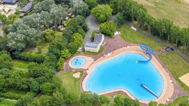 An aerial view of a residential area with a large swimming pool, surrounded by lush greenery and a few houses.