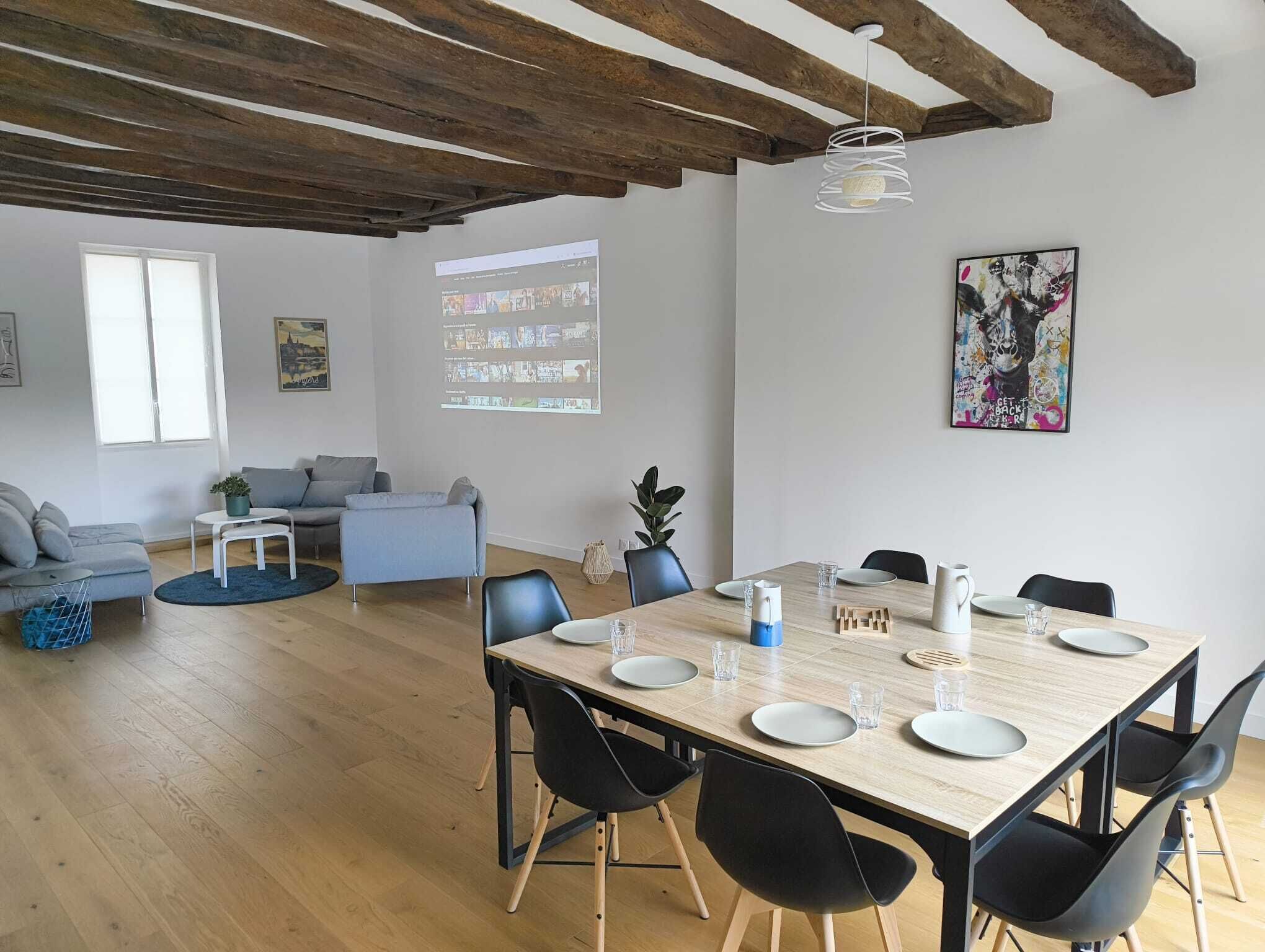 A modern living room with a dining area, wooden flooring, and exposed beams on the ceiling.