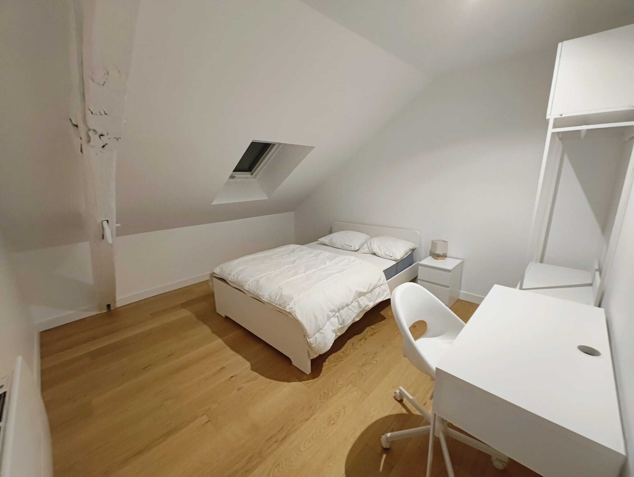 Une chambre à coucher comprenant un lit, un bureau, une chaise, une table de chevet et une lucarne.