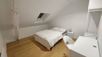 Une chambre à coucher comprenant un lit, un bureau, une chaise, une table de chevet et une lucarne.